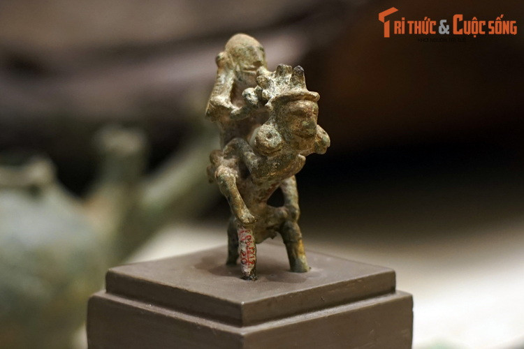 Tượng cao 8,5 cm, rộng: 9,5 cm thể hiện cảnh hai người cõng nhau. Người cõng tóc vấn búi cao, tai đeo khuyên tròn, hai tay choàng ra, ôm đỡ người ngồi trên lưng. Người ngồi trên lưng miệng ngậm khèn, một tay ôm lấy người cõng, một tay đỡ lấy khèn.