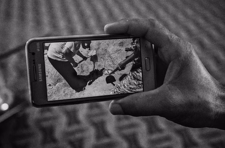 Một chiến binh chính phủ Libya đưa điện thoại ra cho phóng viên xem cảnh đào ngôi mộ tập thể phía sân sau nhà tù này.