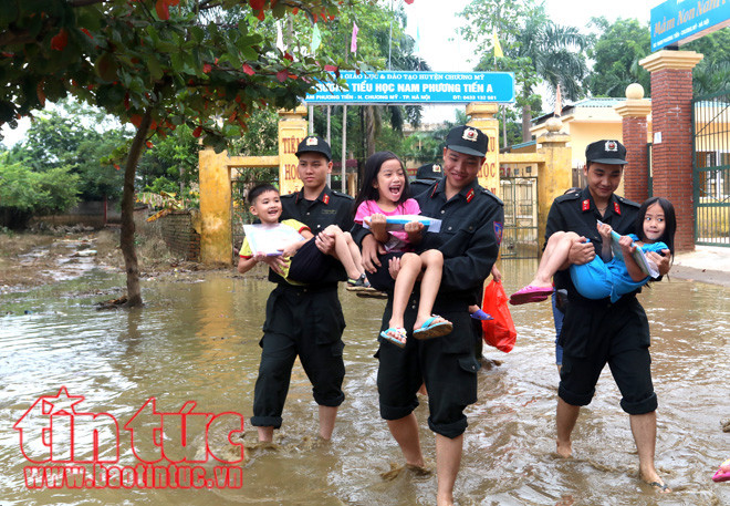 Các em nhỏ được các chiến sĩ cảnh sát cơ động bế qua vũng nước ngập sâu trước cổng trường.