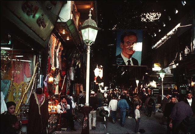 Khung cảnh náo nhiệt tại một khu chợ ở Damascus. Ảnh chân dung cỡ lớn của Tổng thống thời đó là ông Bashar được treo tại khu vực trung tâm chợ. (Ảnh Ifeng)