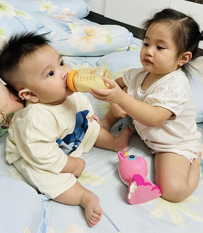 Chị Ba giúp bố mẹ cho em trai út uống sữa.