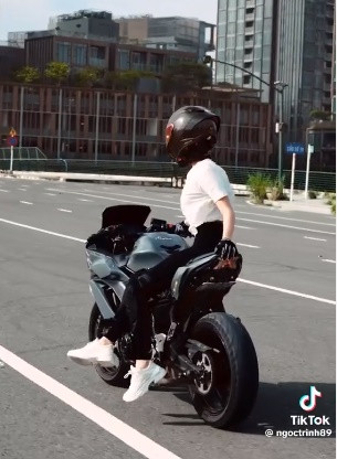 Ngọc Trinh thể hiện màn thả hai tay, đặt hai chân lên yên xe, ngồi một bên, buông một tay lái xe...