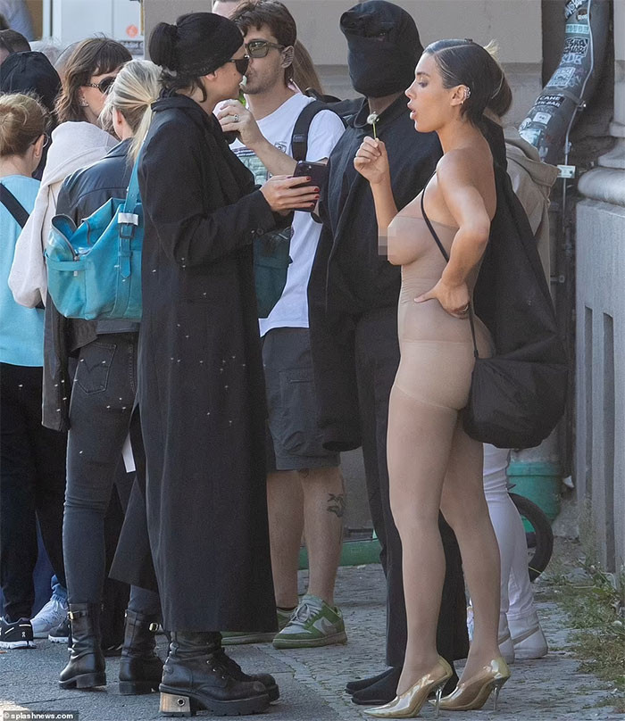 Kanye West trùm kín đầu và mặt bằng một chiếc khăn đen, quần áo cũng màu đen. Vợ anh vẫn như mọi khi, khoe vòng một khủng trong bộ đồ bó sát màu da. (Ảnh: Splasnews)