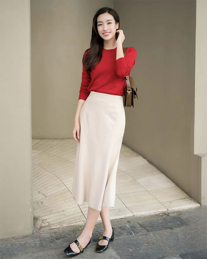 Đỗ Mỹ Linh trang nhã khi diện chân váy màu kem kết hợp với áo len mỏng màu đỏ và nhấn nhá là đôi giầy đen, chiếc túi xách hàng hiệu. (Ảnh: FBNV)