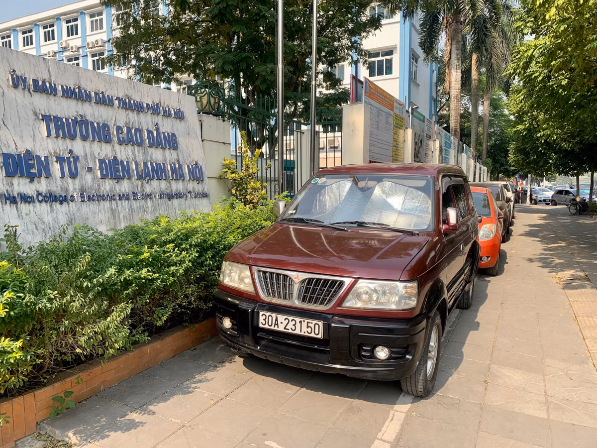 Xe ô tô đỗ, xếp hàng dài trên vỉa hè trước cổng Trường Cao đẳng Điện tử - Điện lạnh Hà Nội (Số 10, đường Nguyễn Văn Huyên, Dịch Vọng, Cầu Giấy).