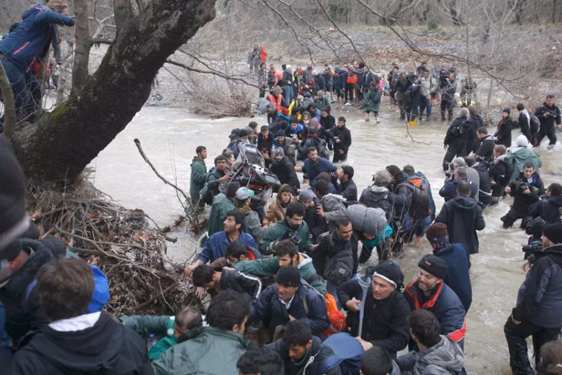 Lực lượng tình nguyện của Hy Lạp và quốc tế giúp di dân lội qua dòng sông chảy xiết bằng một sợi dây thừng.