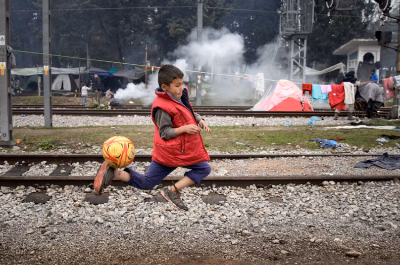 Tuy nhiên, hầu hết những người này đã bị lực lượng an ninh Macedonia đưa vào xe tải để trở về Hy Lạp. Ảnh: Một bé trai chơi đá bóng gần đường ray tàu trong khu trại.