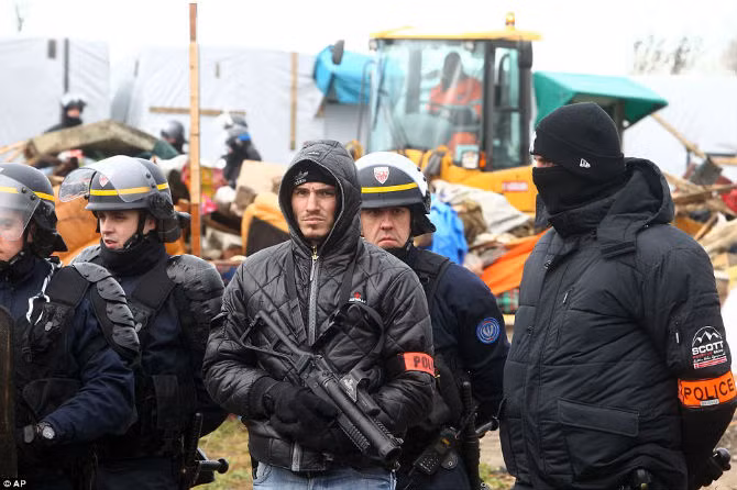 Cảnh sát tuần tra khu vực trong khi các công nhân điều khiển máy ủi, máy đào đất phá dỡ những túp lều tạm bợ.