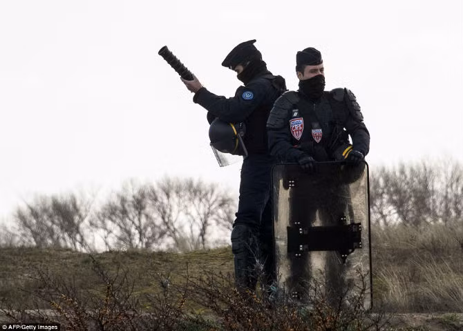 Cảnh sát trang bị súng phóng hơi cay, dùi cui, khiên,... đứng gác quanh khu trại trị nạn Jungle.