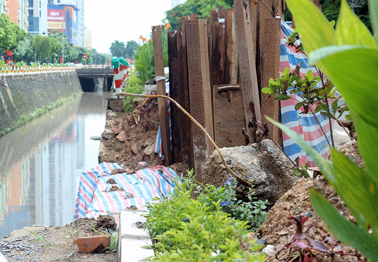 Để ngăn đất không tiếp tục bị sạt lở và thuận tiện cho việc sửa đường, đơn vị thi công đã tiến hành đóng cọc dầm sắt, lấy bạt chắn ở phía mép đường nhựa.