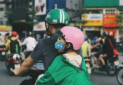 Ngày 12/6, khoảnh khắc cảm động tài xế Grab Bike tranh thủ đón con về, cậu bé ngủ gà gật nên ông bố buộc áo đồng phục quanh người con vừa che nắng, vừa để đứa trẻ không bị rơi trở thành tâm điểm chú ý. Ảnh: Pany Chi.