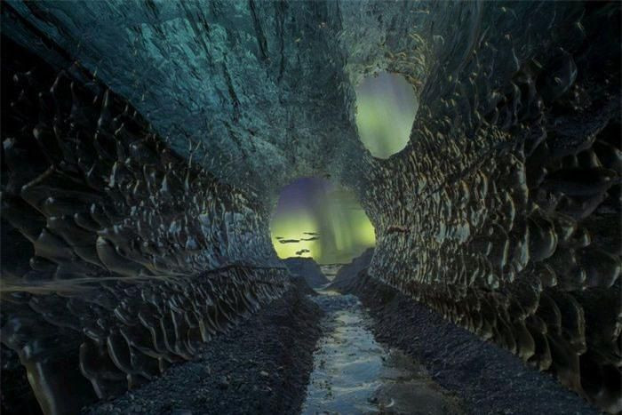 Hình ảnh cực quang xuyên qua một hang động ở Iceland. Băng giá đang hình thành trong lòng hang động tạo nên đường dẫn thị giác độc đáo hướng về cực quang sáng chói nơi cửa hang. Tác giả: Markus van Hauten.