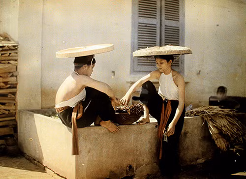 Hai thiếu nữ với áo yếm, quần đen, thắt lưng đỏ và nón ba tầm.