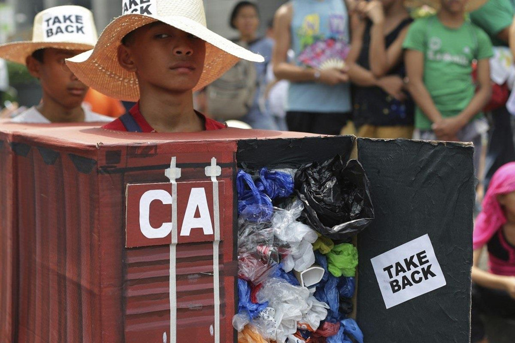 Các nhà hoạt động môi trường mặc một thùng chứa giả chứa đầy rác để tượng trưng cho 50 thùng rác được chuyển từ Canada đến Philippines hai năm trước. Ngày 1/7, trưởng làng Mario San Andres đã cho chủ sở hữu của STC Enterprises, Wilson Uy, hai tuần để dọn dẹp hoặc có nguy cơ mất giấy phép kinh doanh. Ảnh: AP.