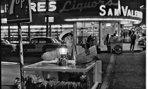 Hình ảnh người bán hàng rong món bánh tacos tại Tijuana. Tacos là món bánh truyền thống lâu đời ở Mexico, được nhiều người biết đến. Trong lúc vắng khách, người bán hàng tranh thủ đọc báo. Ảnh chụp năm 1964.