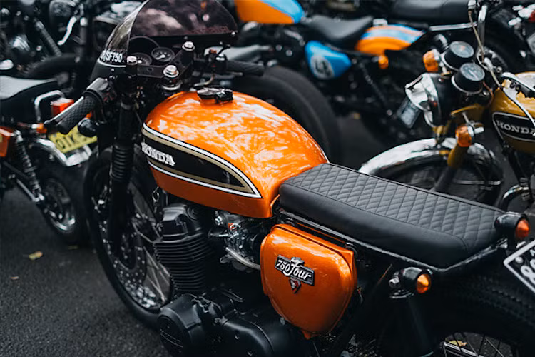 Một chiếc Honda CB750 Four nổi bật với phong cách Brat và tông màu tương phản cam ánh kim/đen mờ.