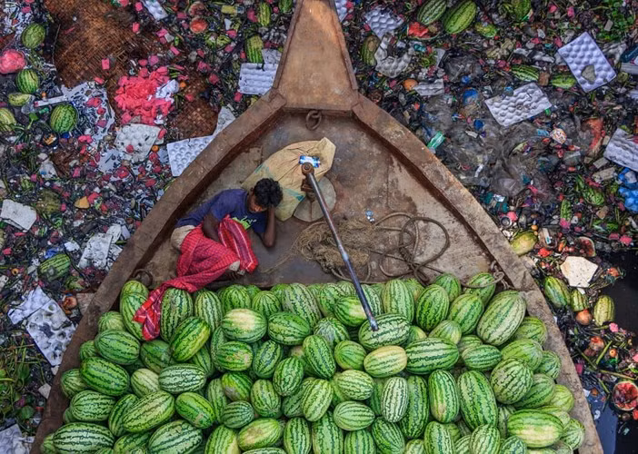 Chiếc thuyền và người bán dưa hấu trôi dạt trên dòng sông Burigongga bị ô nhiễm nặng nề ở Dhaka, Bangladesh
