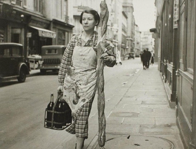 Một người phụ nữ Pháp cầm chiếc bánh mì và 6 chai rượu vang trên đường phố Paris năm 1945.