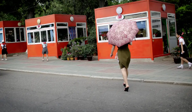 Người phụ nữ cầm ô đi về phía các ki ốt bán đồ ăn, đồ uống ở Bình Nhưỡng.