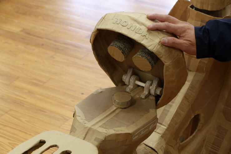 Bên dưới yên xe trước có một khớp bản lề với trục gỗ. Khi mở lên sẽ thấy được một nắp bình xăng và cả 2 chi tiết cao su giảm chấn yên.