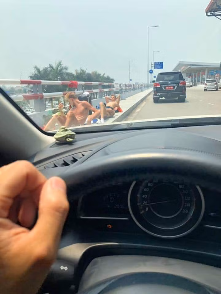 Những hình ảnh vừa được chia sẻ cho thấy nhóm du gồm 4 nam thanh niên. Cả 4 người đều cởi trần, mặc quần đùi, vô tư nằm ngay trên dải phân cách bằng bê tông bên trong khuôn viên sân bay. Những chiếc ba lô hành lý to kềnh càng mang theo được nhóm du khách này dùng làm gối, sau đó cả nhóm cứ thế nằm "phơi nắng" giữa lúc nhiệt độ ngoài trời có thể lên tới trên 40 độ C.