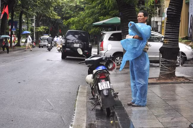 Nhiều người đi đường phải dừng lại mặc áo mưa vì những cơn mưa bất chợt, lúc to, lúc nhỏ.