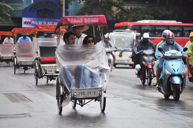 Hai du khách nước ngoài đi xích lô phải quàng thêm áo mưa để tham quan Hồ Gươm.
