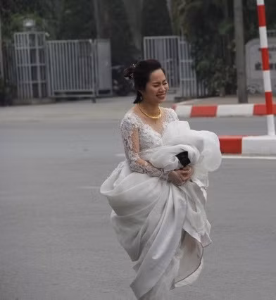 Cô dâu ôm váy đi bộ về nhà chồng. Do đoạn đường bị cấm khá xa nên cô đã nhăn mặt mệt mỏi.