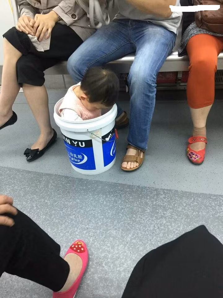Chẳng rõ do không muốn con nghịch trên tàu điện ngầm hay đây là cách giữ con hay ho nhất nên cặp vợ chồng trên ảnh đã thản nhiên bắt con ngồi im trong chiếc xô 20 lít.
