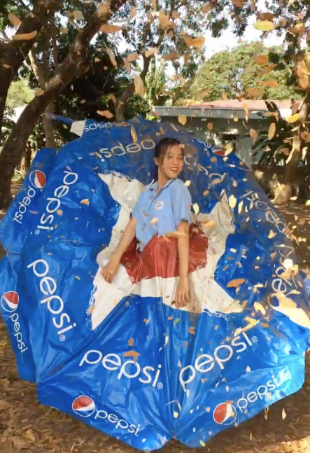 Vấn đề là Cẩm Tiên không chụp ảnh ở studio với trang phục cầu kì được chăm chút mà bối cảnh là ngay sân trường. Bộ trang phục của cô nữ sinh lớp 11 này còn khiến nhiều người sốc đó là chiếc ô quảng cáo nước giải khát bị bỏ không ở góc sân trường.