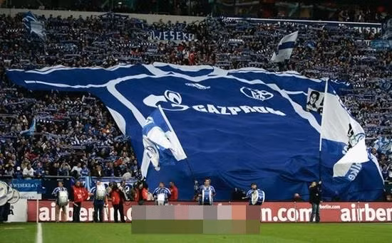 Các CĐV Schalke vào sân Veltins Arena mang chiếc áo khổng lồ của đội bóng lên khán đài để cổ vũ đội nhà.