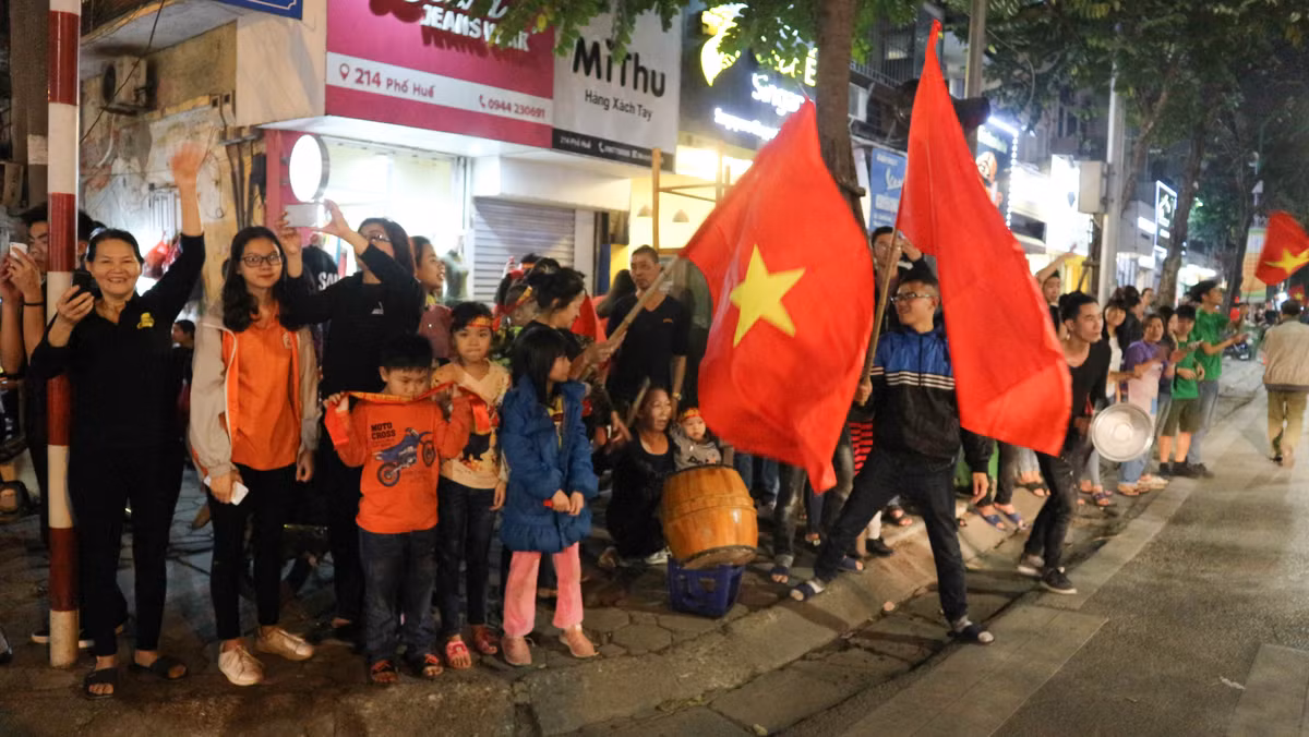 Ở một góc đường phố Lê Văn Hưu giao với phố Huế, một nhóm các em nhỏ đã ra đường cổ vũ dòng người ăn mừng chiến thắng của U23 Việt Nam. Các em tay cầm trống, tay cầm cờ liên tục tạo ra những âm thanh vô cùng sinh động