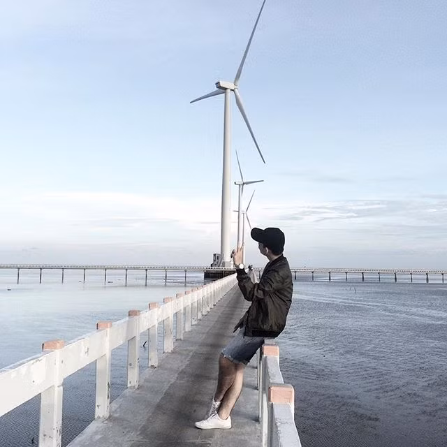 Từ thành phố Bạc Liêu theo đường Cao Văn Lầu đi ra phía biển, ở địa phận ấp Biển Đông A, xã Vĩnh Trạch Đông là Nhà máy điện gió mới được hoàn thành đầu năm nay. Khoảng cách từ trung tâm thành phố đến nhà máy khoảng gần 20km, nhưng từ cách xa cả chục cây số, bạn đã có thể nhìn thấy những trụ turbine lắp cánh quạt quay đều như những chong chóng khổng lồ in trên nền trời. Đây là điểm chụp ảnh yêu thích của nhiều bạn trẻ khi đến với Bạc Liêu. Ảnh trong bài: Instagram Kkelvinyuenn.