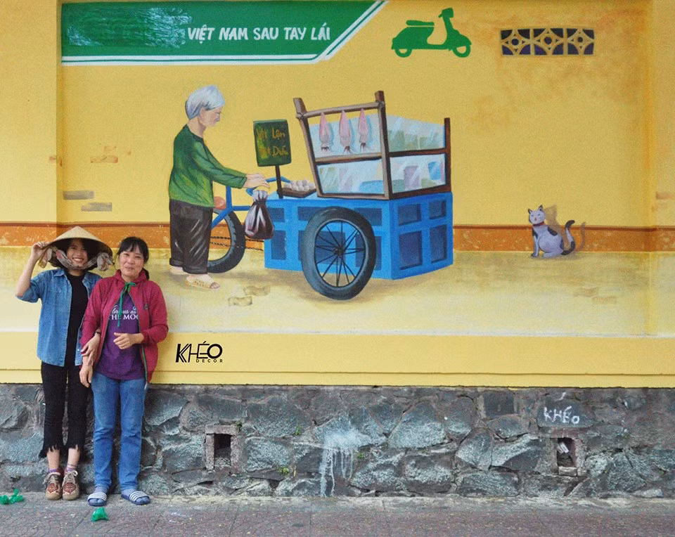 Sự phấn khích của một cô bán hàng rong nơi bức tường được các bạn trẻ nhóm "Việt Nam sau tay lái" thực hiện sơn sửa. Ảnh trong bài: KIds Dương.