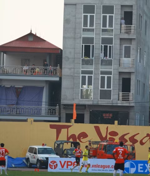 Không nguy hiểm như việc trèo lên nóc nhà, các khán giả ở Ninh Bình chỉ dám dừng lại ở việc ngồi ở hành lang và nhìn ra sân bóng. Ảnh: Bongdaplus.