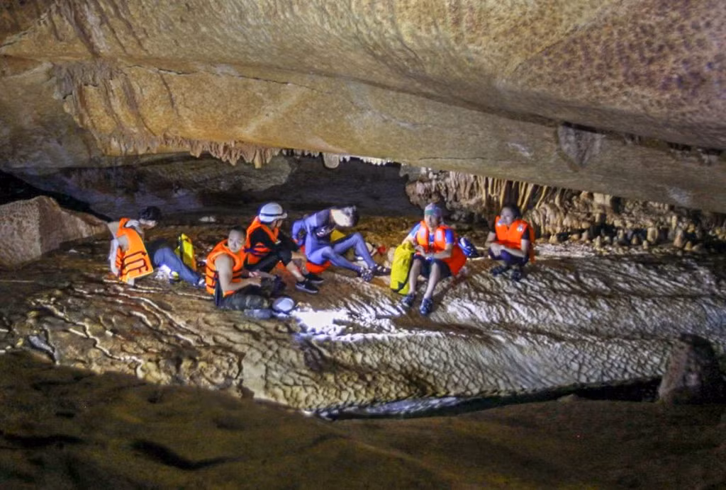 Bò qua đoạn hang thấp, chúng tôi tới một phòng hang rộng khoảng 100 m2, và không thấy đường đi tiếp, nên cả đoàn ngồi nghỉ, ăn trưa. Một vài thành viên trong đoàn tranh thủ đi trước dò đường.