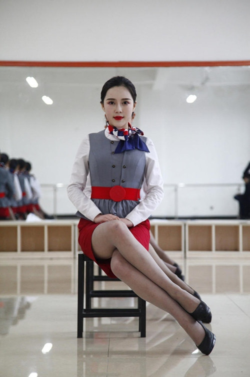 Các nữ học viên hàng không phải học các tư thế tạo dáng trong khóa học làm tiếp viên như ngồi chéo đùi, đầu ngẩng cao, tóc bới gọn vàng và miệng cười mỉm.