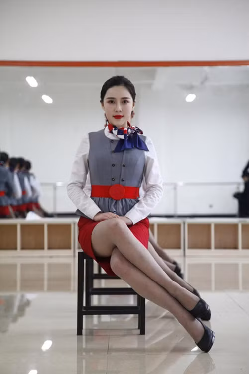 Các nữ học viên hàng không phải học các tư thế tạo dáng trong khóa học làm tiếp viên như ngồi chéo đùi, đầu ngẩng cao, tóc bới gọn vàng và miệng cười mỉm.