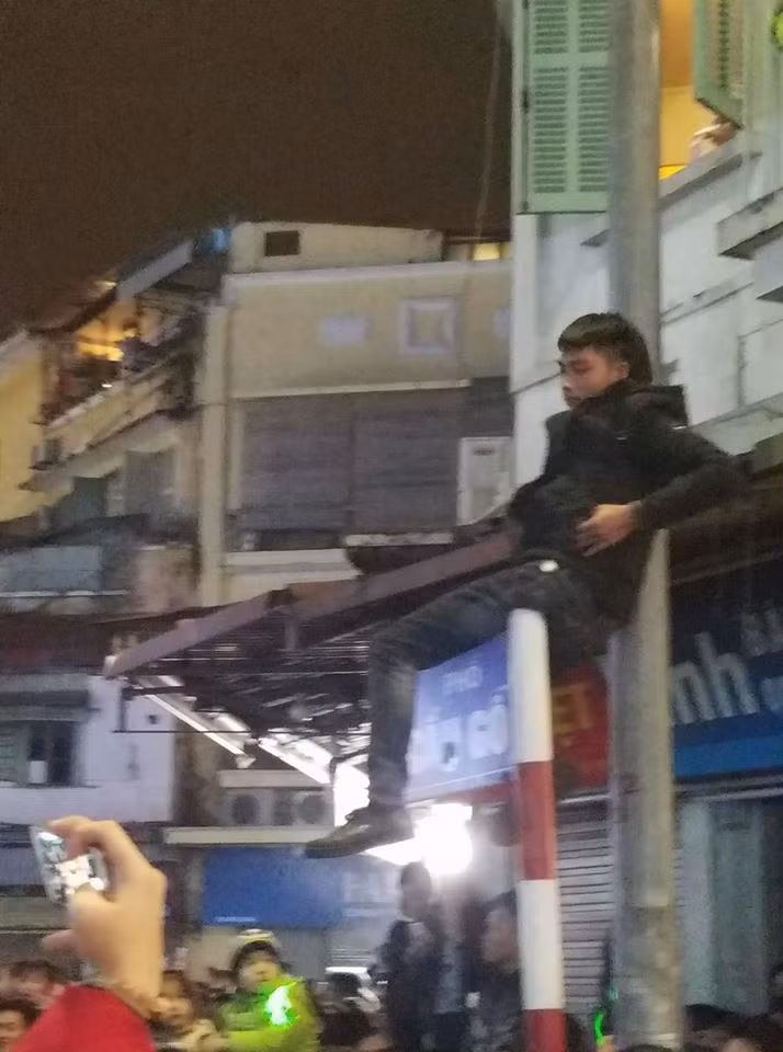 Bá đạo hơn nữa, ở góc phố Cầu Gỗ, một thanh niên còn táo bạo hơn khi trèo lên cột biển ghi tên phố để tận hưởng phút giây sôi động.