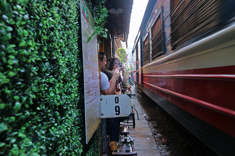 Các vị khách đứng nép sát vào những khu nhà dọc đường tàu để chụp những bức ảnh khi có đoàn tàu chạy qua.