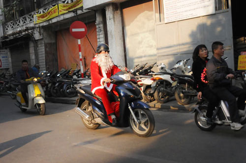 Trước đó, tại Việt Nam cũng xuất hiện rất nhiều ông già Noel làm nhiệm vụ giao quà trong dịp Giáng sinh. Ông Thái Duy Anh ( 57 tuổi) tại Hà Nội, dù bận trăm công ngàn việc nhưng vẫn tranh thủ dành thời gian tới hàng Mã - nơi có cửa hàng bán đồ trang trí của con gái để nhận các món quà chuẩn bị đi phát cho các em nhỏ. Ảnh: Dân Việt.