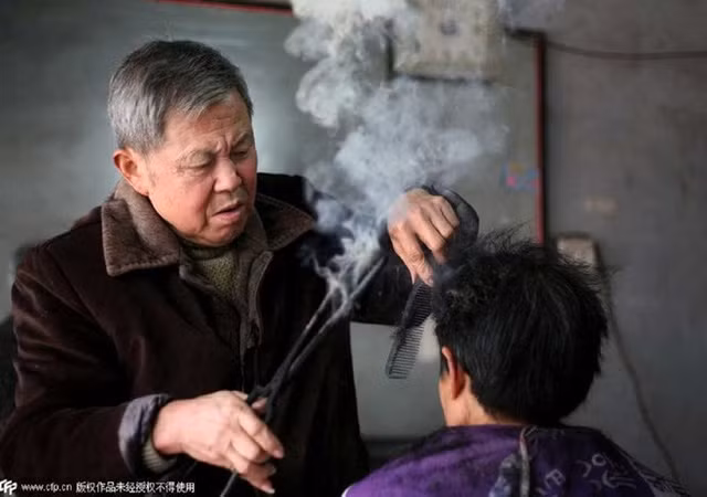 Không cần đến máy ép hay máy là, người thợ cắt tóc Trung Quốc trên dùng chiếc kẹp than để ép tóc cho khách hàng của mình.