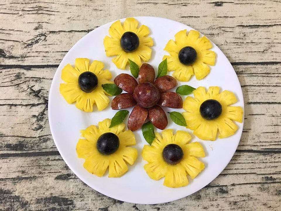 "Tổ hợp hoa" được làm từ mận, dứa và nho đen. Bạn chỉ cần cắt dứa thành khoanh tròn, bổ một quả mận kiểu mo cau và sắp xếp trên một đĩa trắng như hình.
