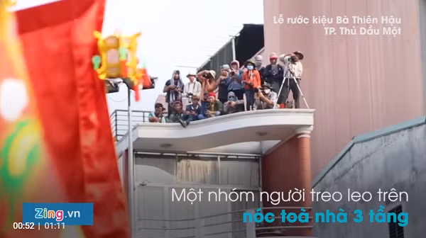 Chiều 2/3, thời tiết oi bức nhưng hàng nghìn người dân Bình Dương và du khách nhiều tỉnh miền Tây khác vẫn đứng chờ đoàn rước kiệu chùa Bà Thiên Hậu đi qua để hứng lộc, xem các màn biểu diễn. Trong lễ hội rước kiệu, nhiều người đã mạo hiểm leo lên hàng rào, trụ cột, nhà cao tầng cách mặt đất 4-5 m để có vị trí xem rước kiệu rõ ràng. Những địa điểm này không có rào chắn bảo vệ nhưng nhiều phụ huynh thậm chí còn kéo trẻ em lên. Ảnh: Zing.vn
