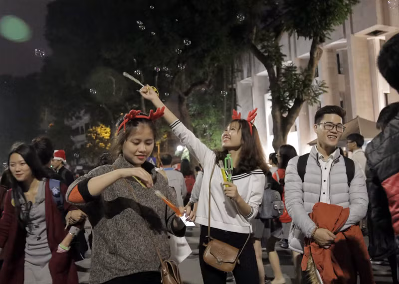 Hai bạn gái xinh đẹp vui vẻ với trò chơi bong bóng xà phòng trên phố đi bộ Hồ Gươm đêm trước ngày Noel.