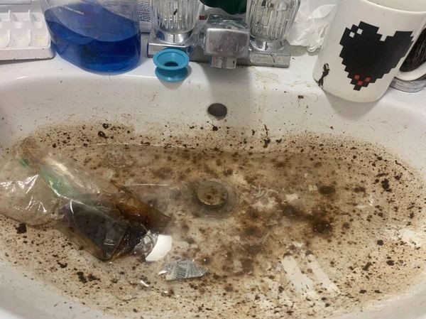 Bồn rửa mặt nghẹt nước, đầy rác và cặn bẩn.