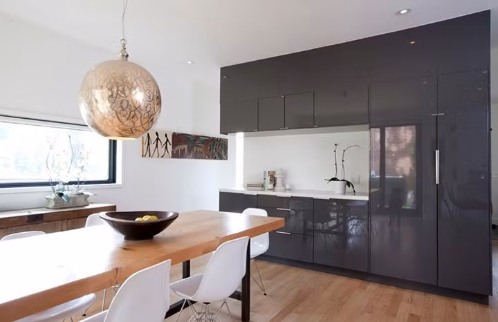 Bàn ăn bằng gỗ ở đây phù hợp với màu sắc sàn nhà. Tủ bếp tương phản tốt với tường trắng.