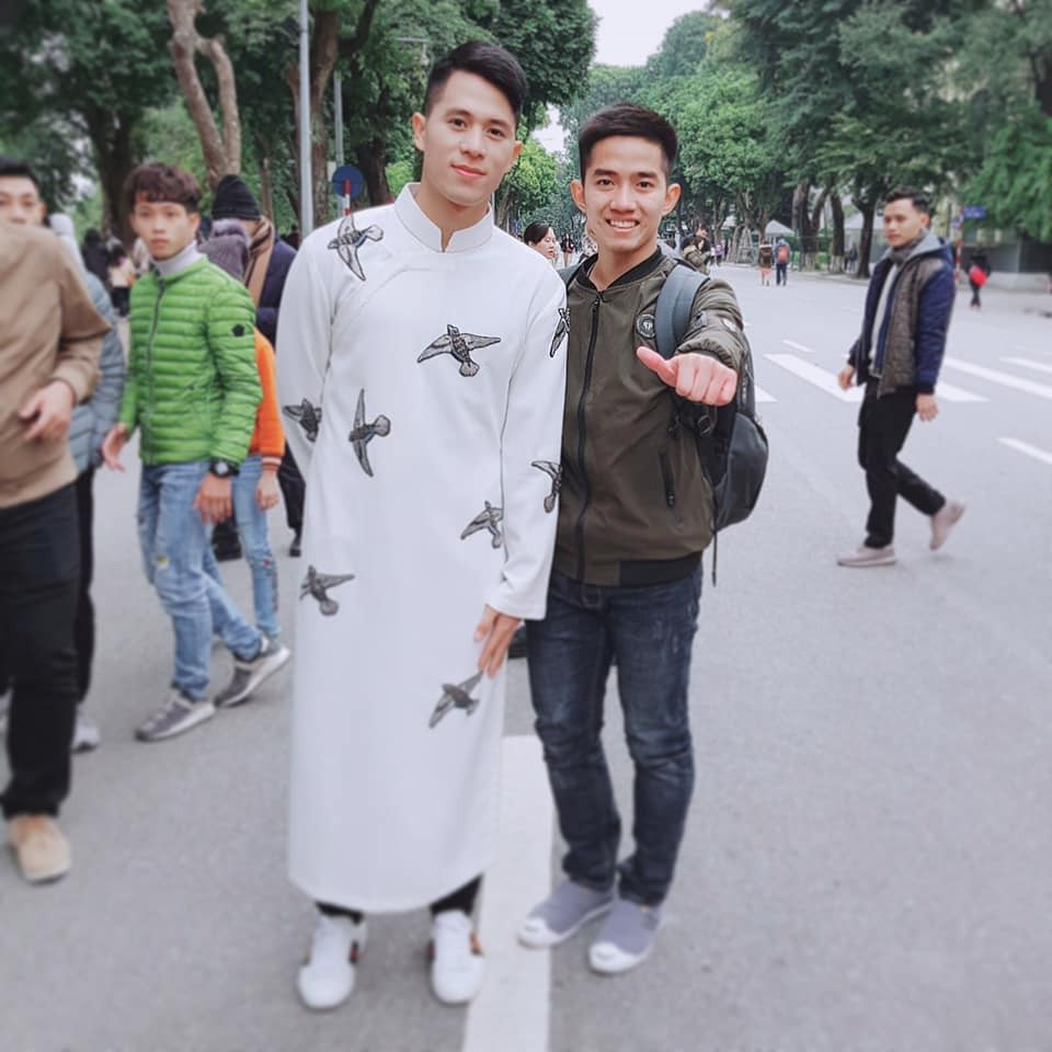 Đình Trọng cùng Văn Quyết diện áo dài với quần jeans phóng khoáng. Mẫu áo đính kết cánh chim én, vẹt rực rỡ sắc màu nổi bật trên nền màu kem nhạt, chất liệu thô đũi khỏe khoắn, năng động đúng với tính chất của những cầu thủ.