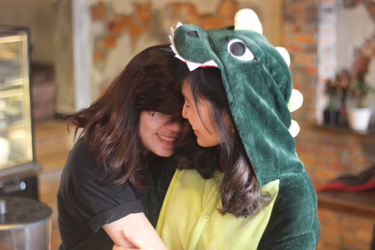 Một nữ nhân viên xinh đẹp của quán đã được cử để mặc bộ đồ mascot hình chú khủng long xanh lá để ôm từng vị khách khi đến quán. Ảnh: FB Cafe Ôm.