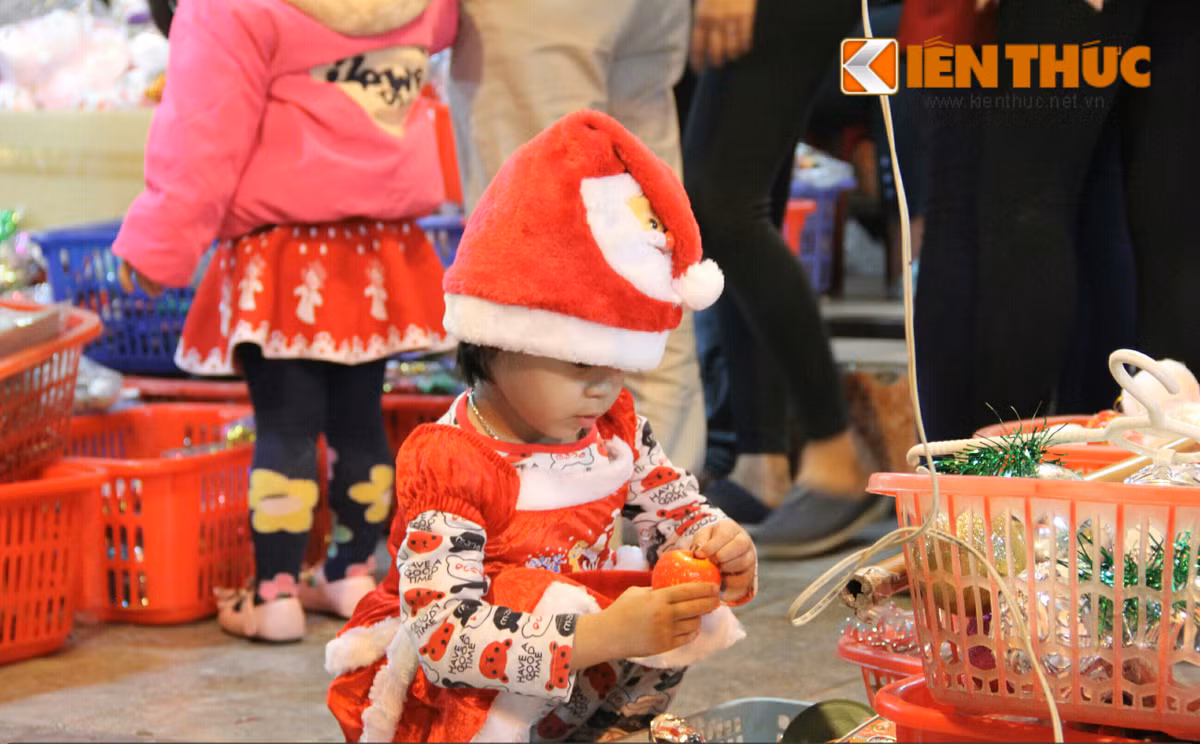 Ảnh một em bé dễ thương trong bộ quần áo Giáng sinh đang ngồi chơi những vật trang trí Noel trên phố Hàng Mã - Hà Nội.